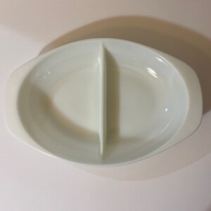 May include: White oval divided serving dish with a center divider. The dish has a smooth, glossy finish.