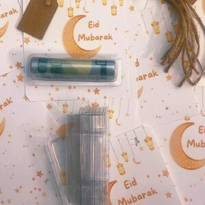 Könnte beinhalten: Eine Auswahl an Eid Mubarak-Grußkarten mit Mond- und Laternenmotiven. Braune Geschenkanhänger und ein transparenter Kunststoffbehälter mit einem Produkt sind ebenfalls vorhanden. Der Text "Eid Mubarak" ist sichtbar.