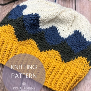 Puede incluir: Un gorro tejido con un patrón en zigzag en colores mostaza, verde oscuro, azul marino y crema. El texto "KNITTING PATTERN" es visible en la parte inferior izquierda del gorro. El gorro está hecho de hilo grueso.