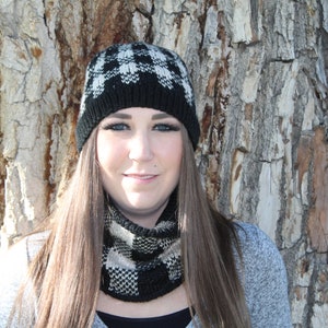 May include: A black and white checkered knit hat and matching neck warmer. The hat has a folded brim and the neck warmer is a cowl style.