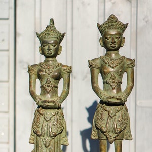 Könnte beinhalten: Zwei grüne Bronzestatuen von Figuren, die kunstvolle Kopfbedeckungen und aufwendige Kleidung tragen, stehen auf schwarzen Sockeln.