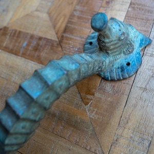 Könnte beinhalten: Ein dekorativer Türgriff aus Metall mit einem strukturierten, schuppigen Design. Der Griff ist dunkelblau-grau und hat eine abgerundete Oberseite.