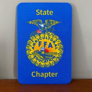 May include: A blue rectangular FFA State Chapter emblem with rounded corners. The emblem features a yellow eagle, owl, and sun design, with the words "AGRICULTURE" and "EDUCATION" in a circular pattern. The words "State" and "Chapter" are in yellow.