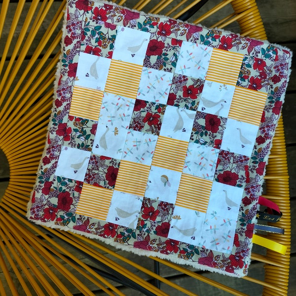 Doudou plat carré en tissu façon patchwork avec jolis motifs  dans les tons rouge et jaune et un côté en tissu polaire tout doux