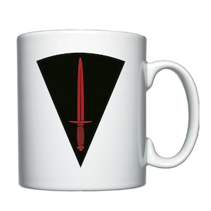 May include: White ceramic mug featuring a black triangle with a red dagger inside. The dagger has a black handle with a white spiral design.