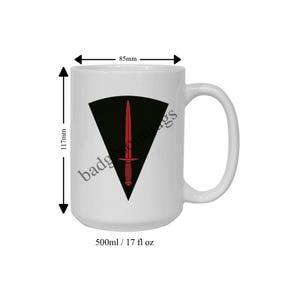 May include: White ceramic mug with a black and red dagger logo. The logo is a black triangle with a red dagger inside. The mug is 500ml and has a handle on the right side.