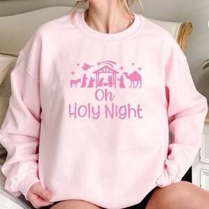 K&ouml;nnte beinhalten: Rosafarbener Pullover mit einem rosafarbenen Motiv einer Weihnachtskrippe und dem Text "Oh Holy Night".