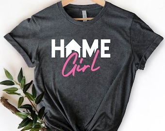 Może przedstawiać: Szary t-shirt z nadrukiem "HOME Girl" w kolorze białym i różowym. Słowo "HOME" ma ikonę domu zamiast "O".