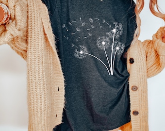 May include: A dark grey t-shirt featuring a white dandelion design. The shirt is styled with a beige cardigan.