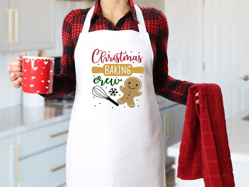 May include: White apron with the text "Christmas Baking Crew" in red and green lettering. A gingerbread man cookie and a rolling pin are also featured on the apron.