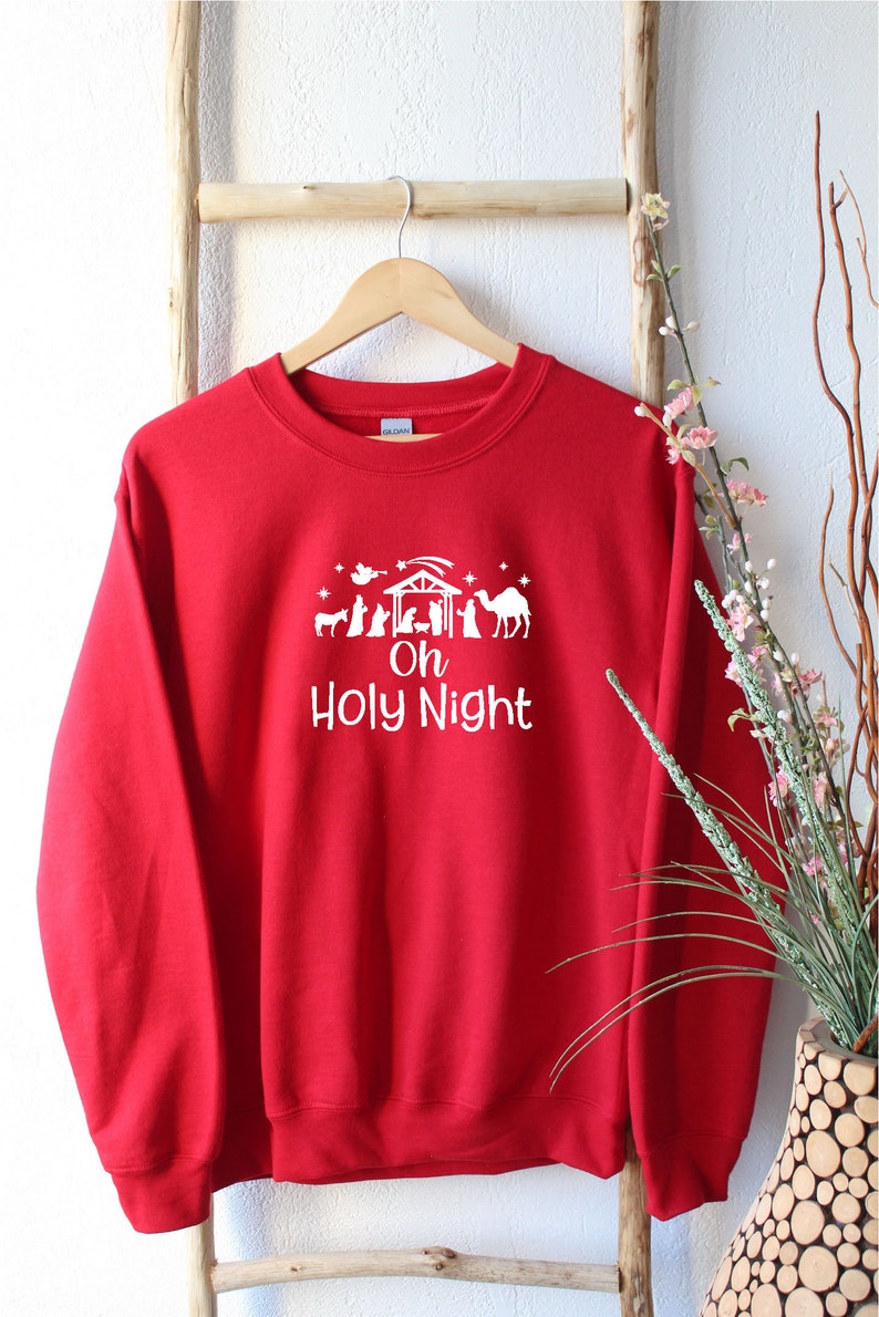K&ouml;nnte beinhalten: Roter Weihnachtspullover mit einem wei&szlig;en Design einer Weihnachtskrippe und dem Text "Oh Holy Night".