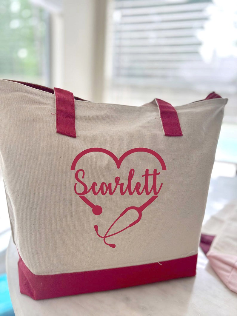 May include: A white canvas tote bag with red handles and a red heart design. The heart has a stethoscope inside and the name "Scarlett" written inside the heart.