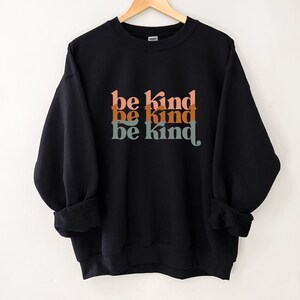 May include: Black sweatshirt with the phrase "be kind" repeated three times in a retro font with orange, brown, and green colors.