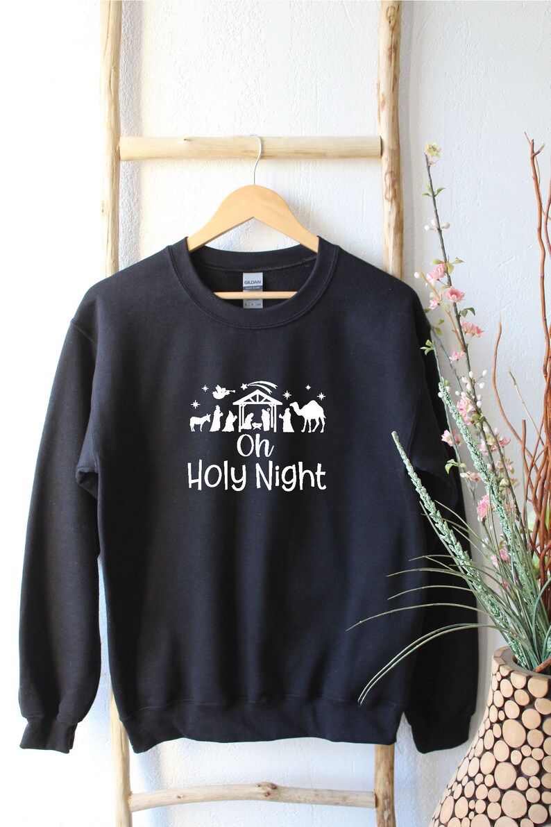 K&ouml;nnte beinhalten: Schwarzer Pullover mit einem wei&szlig;en Aufdruck einer Weihnachtskrippe und dem Text "Oh Holy Night".