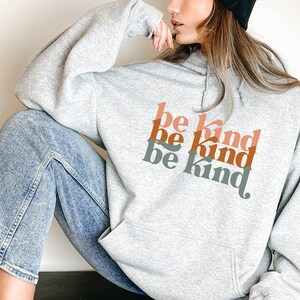 May include: A gray hoodie with the phrase "be kind" repeated three times in a retro font. The text is in shades of orange, pink, and green.