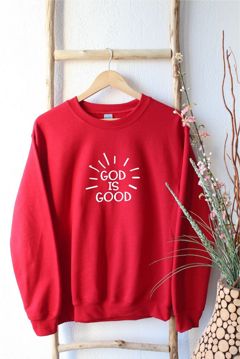 May include: Red sweatshirt with a white graphic that says "God is Good" with radiating lines around the text.