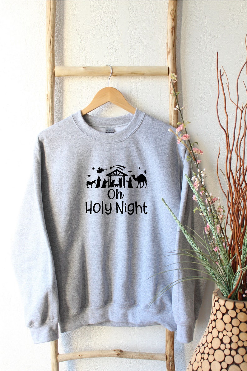 K&ouml;nnte beinhalten: Ein graues Sweatshirt mit einer schwarzen Silhouette einer Weihnachtskrippe und dem Text "Oh Holy Night".