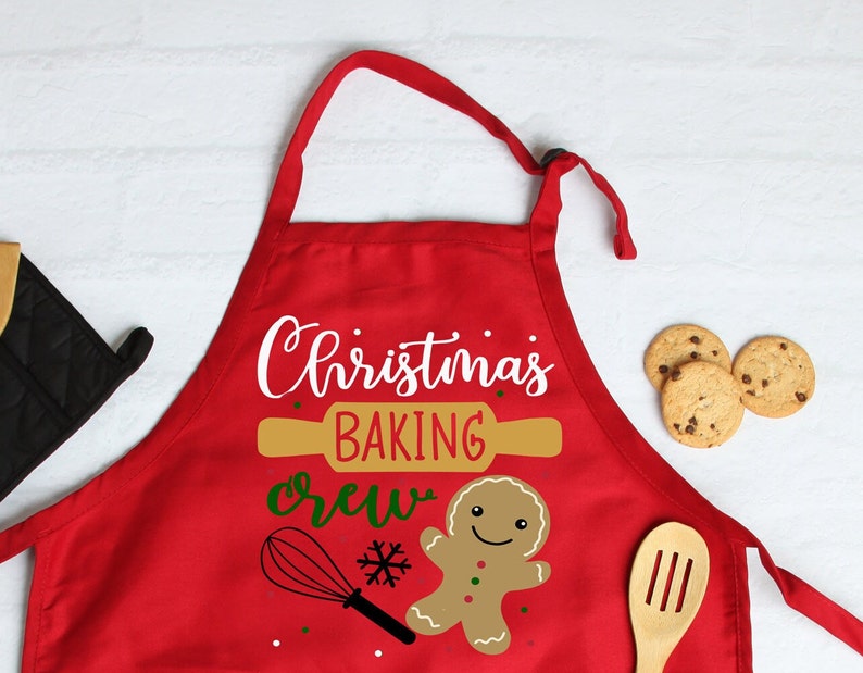 May include: Red Christmas baking crew apron featuring a gingerbread man, a rolling pin, and a whisk. The text on the apron reads "Christmas Baking Crew".