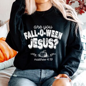 May include: Black sweatshirt with the text "are you FALL-O-WEEN JESUS?" in white, along with a pumpkin graphic and the Bible verse Matthew 4:19. The sweatshirt is a fall-themed item.