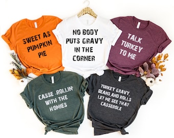 May include: Five different t-shirts with Thanksgiving-themed text printed on them. The shirts are in various colors, including orange, white, maroon, green, and gray. The text on the shirts includes "Sweet as Pumpkin Pie", "No Body Puts Gravy in the Corner", "Talk Turkey to Me", "Casse-Rollin' with the Homies", and "Turkey Gravy, Beans, and Rolls Let Me See That Casserole".