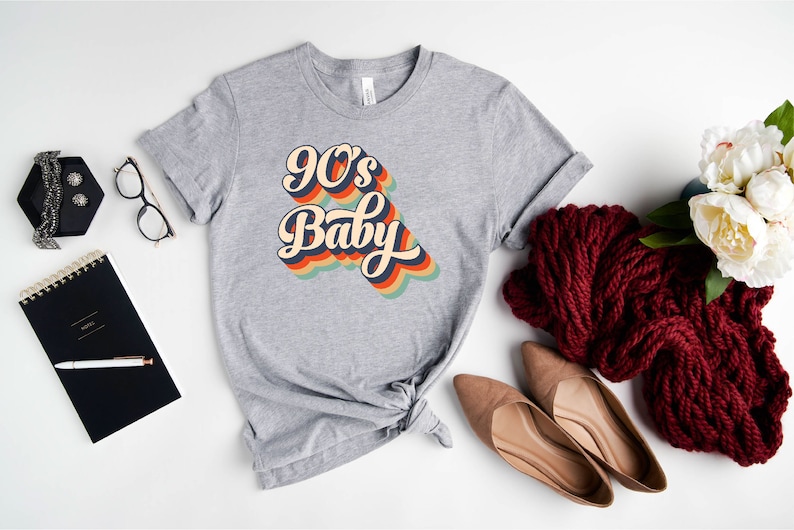 May include: Gray t-shirt with a retro-style graphic that says "90's Baby" in rainbow colors.