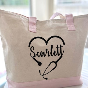 May include: A white canvas tote bag with pink handles and trim. The bag has a black heart design with a stethoscope and the name "Scarlett" inside the heart.