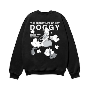 以下が含まれることがあります： 黒いスウェットシャツ。カートゥーンのホットドッグのキャラクターがブリーフケースを持ち、雲の中を歩いているグラフィック。グラフィックの上には「THE SECRET LIFE OF HOT DOGGY」、下には「DELICIOUS THINGS DON'T ASK FOR ATTENTION」と書かれています。