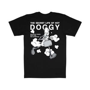 以下が含まれることがあります： 黒いTシャツ。ホットドッグのキャラクターがブリーフケースを持って走っている漫画のイラストが描かれています。「THE SECRET LIFE OF HOT DOGGY」の文字がイラストの上にプリントされ、その下に「DELICIOUS THINGS DON'T ASK FOR ATTENTION」のフレーズがあります。