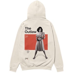 May include: A beige hoodie with a black and white image of a woman in a dress on the back. The image is in a red rectangle with the text "The Outlaw" above it and "A Howard Hughes film" below it. The text "/1943" is at the bottom of the image.
