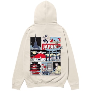 Könnte beinhalten: Ein beiger Hoodie mit einem grafischen Druck verschiedener japanischer Sehenswürdigkeiten und dem Wort "JAPAN" in roten Buchstaben. Zu den Sehenswürdigkeiten gehören der Mount Fuji, der Tokyo Tower, ein Tempel und ein Schrein.