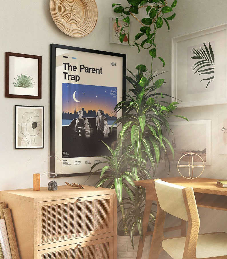 May include: An interior scene featuring framed art, a poster for "The Parent Trap" film, and a wooden cabinet. The room is adorned with plants, a woven wall hanging, and a wooden desk and chair. The colour palette is neutral with natural wood tones.
