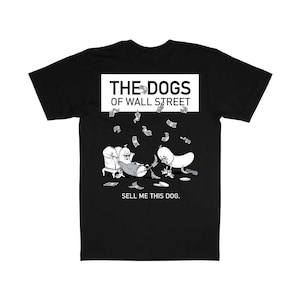 Puede incluir: Camiseta negra con un gráfico que presenta dos perros de dibujos animados rodeados de dinero. El texto "THE DOGS OF WALL STREET" está encima de la ilustración, y "SELL ME THIS DOG." debajo.