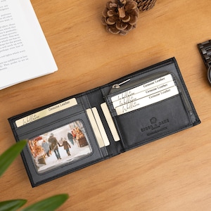 May include: A black bifold wallet made of genuine leather featuring multiple card slots, a clear ID window containing a photograph of people walking in a snowy setting, and a zippered compartment. The wallet is embossed with the brand name Ridge & Jane.