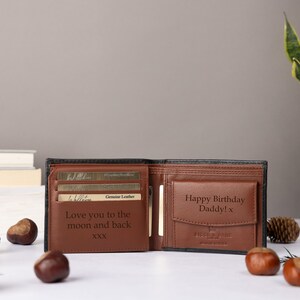 May include: A bi-fold wallet made of black and brown leather, featuring an open interior with card slots and a coin pocket. The interior is engraved with the text 'Love you to the moon and back XXX' and 'Happy Birthday Daddy! x' on the coin flap.