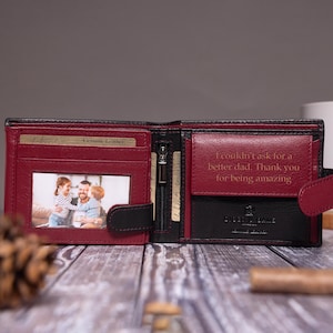 May include: A bi-fold wallet in black and deep red leather. The left side features a clear window containing a photograph of a family. The right side has a flap with the engraved text: I couldn't ask for a better dad. Thank you for being amazing.