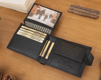 May include: Black leather wallet with multiple card slots and a photo insert. The wallet is open, revealing a picture and several gold-colored cards. A black watch with a dark face is next to the wallet. The wallet is on a wooden surface.