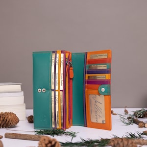 May include: A multi-colored leather wallet featuring a teal exterior and an interior with orange, purple, and yellow accents. The wallet includes multiple card slots, a clear identification window, and a snap button closure for secure storage.
