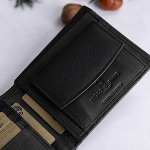 May include: A black leather wallet featuring multiple card slots, a coin pocket with a flap, and the embossed text BIGGS & BATE LONDON GENUINE LEATHER. The interior includes several gold-colored cards labeled Genuine Leather and a plaid fabric lining.