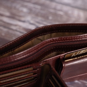 May include: A brown leather wallet with multiple card slots and a zippered compartment. The wallet is open and shows the interior lining.