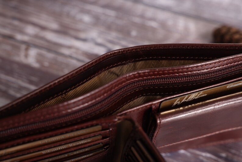 May include: A brown leather wallet with multiple card slots and a zippered compartment. The wallet is open and shows the interior lining.