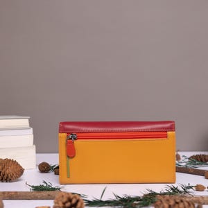 May include: A tri-fold leather wallet with a red, orange, and yellow color scheme. The wallet has a zipper closure and a silver pull tab.