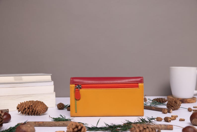 May include: A tri-fold leather wallet with a red, orange, and yellow color scheme. The wallet has a zipper closure and a silver pull tab.