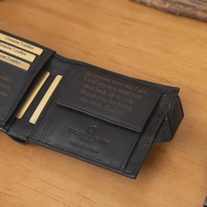 May include: Black leather wallet with engraved text and a matching black wristwatch. The wallet is open, revealing card slots and more engraved text. The watch has a dark face and a black metal band.