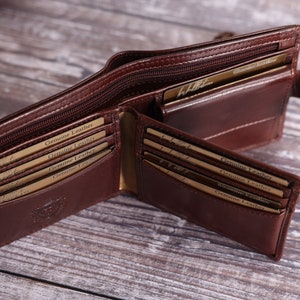 May include: A brown leather wallet with multiple card slots and a zippered compartment. The wallet is open and the interior is visible, showing the card slots and the zippered compartment. The wallet is made of genuine leather and has a logo on the front.