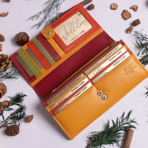 May include: A yellow leather wallet with multiple card slots and a red leather interior. The wallet has a small window for displaying identification and the text "Volluto Genuine Leather" is printed on the front.
