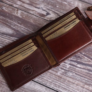 May include: A brown leather wallet with multiple card slots and a zippered compartment. The wallet is open and the inside is lined with a brown fabric. The wallet has a gold embossed logo on the front.