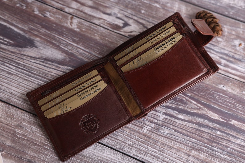 May include: A brown leather wallet with multiple card slots and a zippered compartment. The wallet is open and the inside is lined with a brown fabric. The wallet has a gold embossed logo on the front.