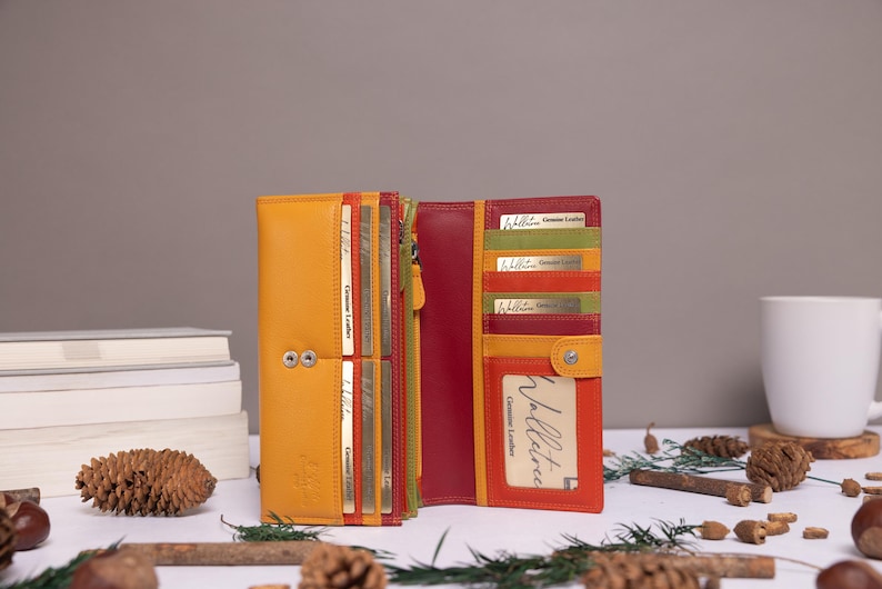 May include: A multi-colored leather wallet with a zipper closure and multiple card slots. The wallet is open and the inside is lined with a red fabric. The wallet has a small window for displaying an ID card. The text "Genuine Leather" is printed on the card slots.