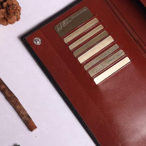 May include: A black leather wallet with multiple card slots. The wallet has a red interior and the text "Genuine Leather" is printed on the inside.