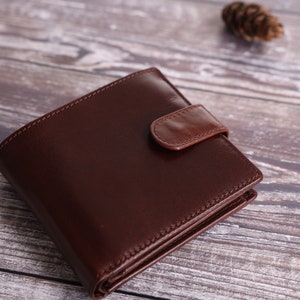 May include: A brown leather wallet with a flap closure. The wallet is folded and lying on a wooden surface.